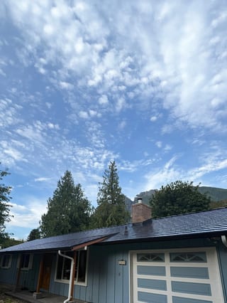 Black Interlock Cedar Shingle aluminum roof on a blue single-family home with a garage door in a forested, North Bend, Washington