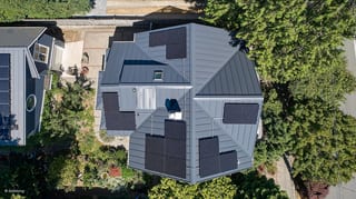 Deep Charcoal Interlock Standing Seam aluminum roof on a two-storey modern home with a metal roof among tall trees, Seattle, Washington