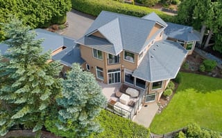Deep Charcoal Interlock Slate aluminum roof on a tan two-storey craftsman home with dormers among tall, Blaine, Washington