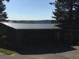 Musket Grey Interlock Standing Seam aluminum roof on a grey two-storey home with dormers among tall pines, Belfair, Washington