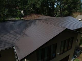 Tudor Brown Interlock Slate aluminum roof on a brown two-storey home with dormers among tall pines, University Place, Washington