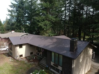 Tudor Brown Interlock Slate aluminum roof on a tan house with a metal roof in a wooded area, University Place, Washington