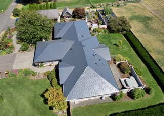 Deep Charcoal Interlock Slate aluminum roof on a grey single-storey ranch-style home among lush greenery, Sequim, Washington