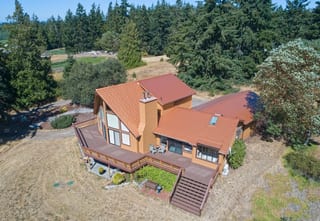 Copper Penny Interlock Cedar Shingle aluminum roof on a two-storey home with a brown metal roof among tall pines, Sequim, Washington