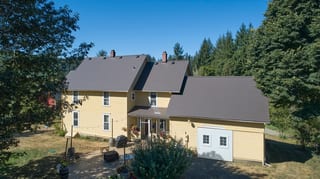 Black Interlock Slate aluminum roof on a yellow two-storey home with dormers among tall pines, Longview, Washington