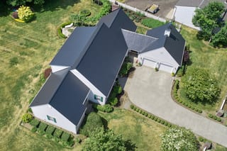 Black Interlock Slate aluminum roof on a white ranch home with a black metal roof among trees, Enumclaw, Washington
