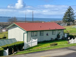 Copper Penny Interlock Cedar Shingle aluminum roof on a white home with green trim and a red roof on a grassy hill, Hoquiam, Washington
