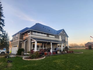 Two-story Craftsman home in rural Buckley, WA with a complex hip roof clad in Interlock deep charcoal aluminum slate tiles at golden hour.