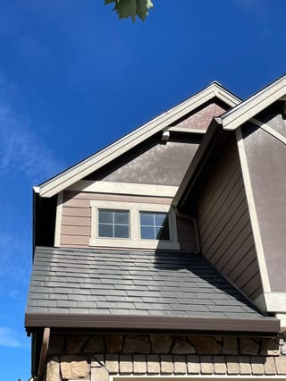 Craftsman home with Interlock Musket Grey aluminum slate roofing featuring a steep dormer, valley, and dark gutters against a vivid blue sky in Vancouver, WA.