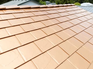 Copper Penny Interlock Slate aluminum roof on a brown two-storey home with a metal roof among tall pines, Castle Rock, Washington
