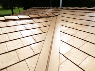 Copper Penny Interlock Slate aluminum roof on a tan two-storey home with dormers among tall pines, Castle Rock, Washington