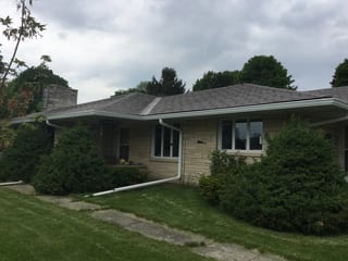 Colonial Brown Interlock Slate aluminum roof on a brown one-storey home with a hip roof among tall pines, Kewaskum, Wisconsin