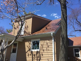 Aged Copper Interlock Slate aluminum roof on a brown one-storey home with a gable roof among tall pines, Watertown, Wisconsin