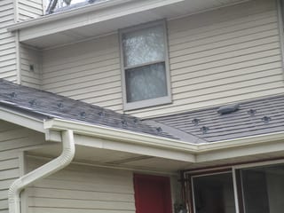 Tudor Brown Interlock Slate aluminum roof on a cream two-storey home with dormers among tall trees, Delafield, Wisconsin