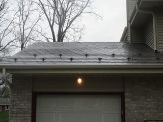 Tudor Brown Interlock Slate aluminum roof on a white Tudor home with dormers among tall pines, Delafield, Wisconsin