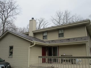 Tudor Brown Interlock Slate aluminum roof on a tan two-storey home with dormers among tall bare trees, Delafield, Wisconsin