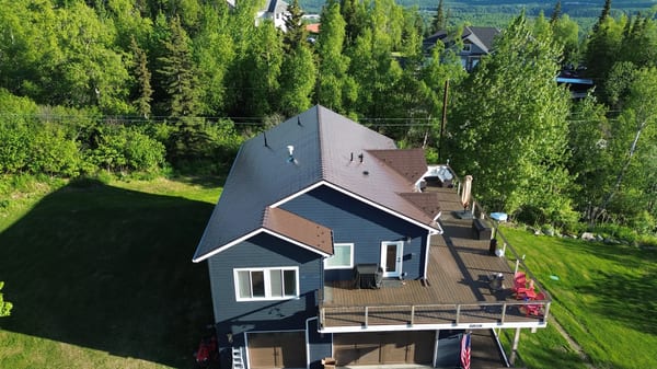 A modern house with a brown metal roof and dark blue siding, surrounded by trees and greenery