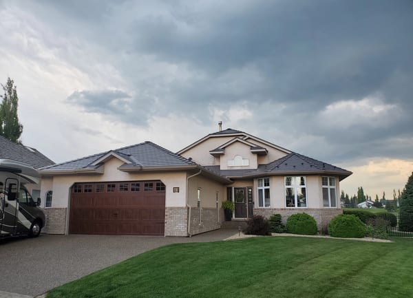 1.5-storey suburban home in Red Deer AB with complex multi-hip Interlock aluminum slate roof in weathered charcoal, stucco exterior, and double garage.