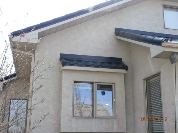 Black Interlock Tile aluminum roof on a beige single-storey home with dormers among tall pines, Redcliff, Alberta