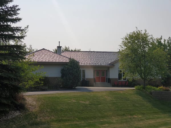 Weathered Interlock Shake aluminum roof on a white ranch home with a red door among tall trees, Sherwood Park, Alberta