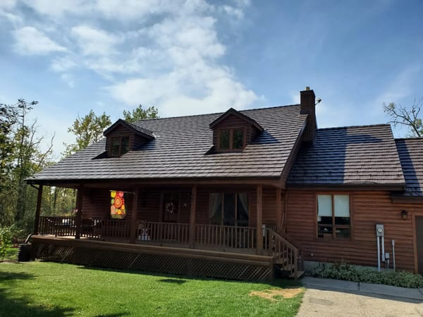 Log-style farmhouse in Red Deer County with Interlock Colonial Brown aluminum shake metal roof, two dormers, chimney, and wraparound covered porch.