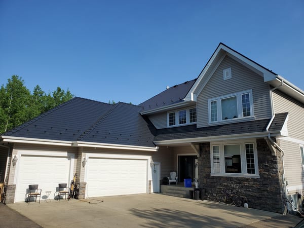 Two-storey Craftsman home in Sherwood Park, AB with black Interlock aluminum cedar shingle metal roof, snow guards, stone accent facade, and triple-car garage.