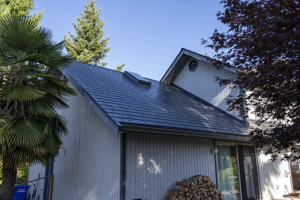 Deep Charcoal Interlock Slate aluminum roof on a white modern home with a metal roof among lush greenery, Sechelt, British Columbia
