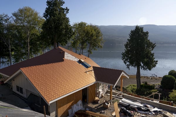 Aerial view of a lakeside cottage with Interlock aluminum slate roofing in Copper Penny, featuring a complex multi-plane roof with skylight and chimney, Sechelt BC.