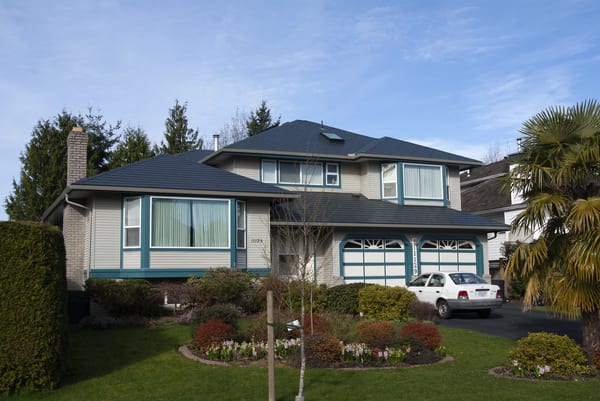 Two-storey suburban home with deep charcoal Interlock aluminum slate metal roof featuring multi-hip complexity, skylight, and teal trim accents in Surrey, BC.