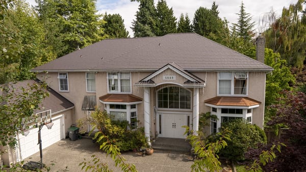 Aerial front view of a two-storey suburban home in Surrey BC with Tudor Brown Interlock aluminum slate roofing, complex hip roof, copper-toned bay window roofs, and brick chimney.