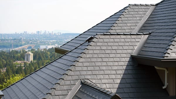 Close-up of a multi-hip deep charcoal Interlock aluminum slate metal roof with complex valleys and ridge caps, overlooking the North Vancouver skyline.