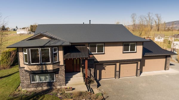 Aerial front view of a Craftsman two-storey home in Abbotsford BC with Interlock deep charcoal aluminum slate metal roofing and complex multi-hip profile.
