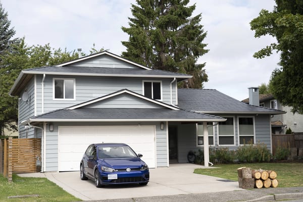 Two-storey suburban home with Interlock deep charcoal aluminum slate metal roofing, multi-plane gable roof, light blue hardie siding, and attached garage in Richmond, BC.