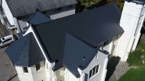 Aerial view of a black Interlock aluminum slate metal roof on a white stucco historic church with complex multi-plane geometry, turrets, and valleys in Vancouver, BC.
