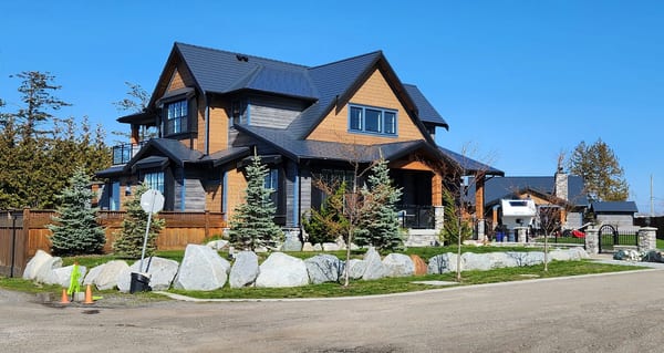Two-storey Craftsman home in Tsawwassen BC with a complex steep Interlock aluminum slate roof in deep charcoal, boulder-lined landscaping, and cedar accents.