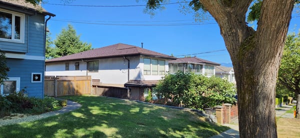 Side elevation of a Burnaby home with Interlock Colonial Brown aluminum shake metal roofing on a hip-style roof under clear blue skies.