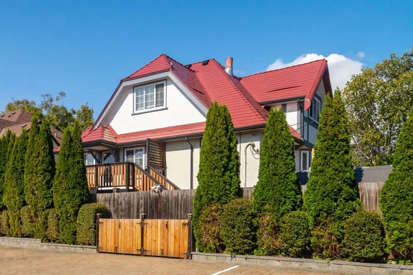 Two-storey Tudor-style home in Victoria BC featuring a complex multi-hip Interlock aluminum slate roof in tile red with dormer, chimney, and cedar privacy hedge.