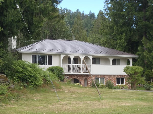 Tudor Brown Interlock Cedar Shingle aluminum roof on a brown one-storey home with a metal roof in a forested, Ladysmith, British Columbia