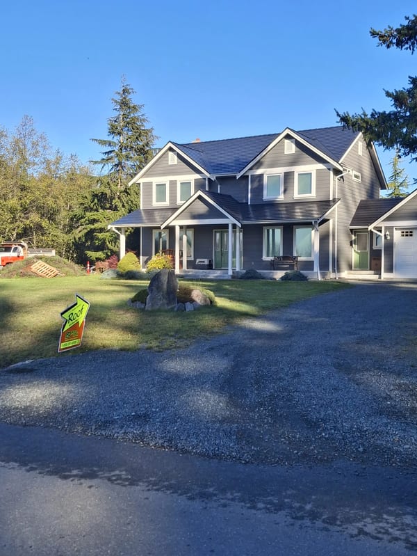 Black Interlock Slate aluminum roof on a two-storey grey home with a metal roof in a forested area, Sooke, British Columbia