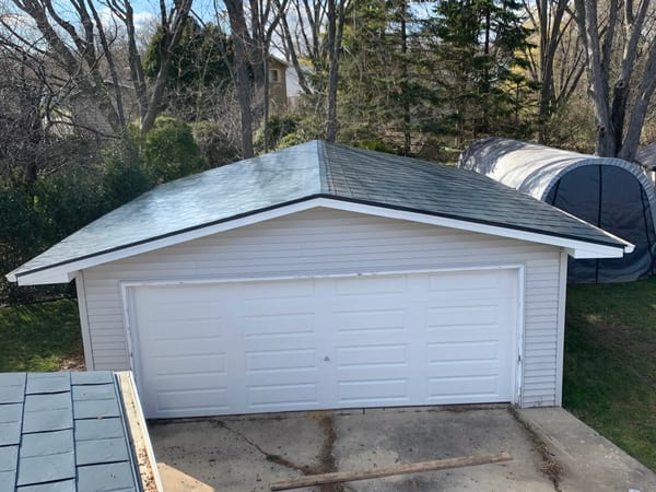 Deep Charcoal Interlock Slate aluminum roof on a white one-storey home with a garage among tall evergreens, Waukegan, Illinois