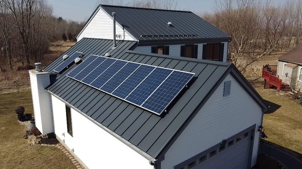 Aerial front view of a farmhouse with Deep Charcoal Interlock standing seam metal roof featuring a large solar panel array and front dormer.
