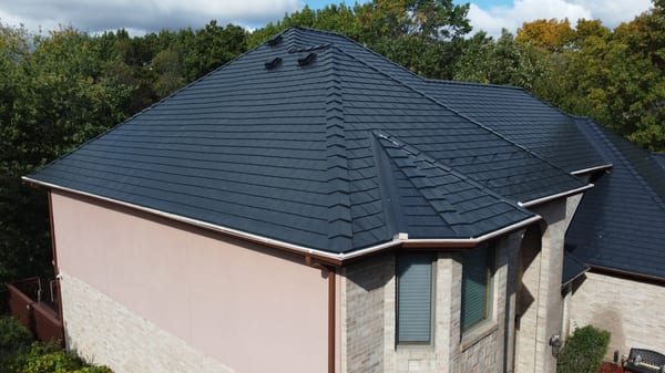 Black Interlock Slate aluminum roof on a beige home with dormers among tall trees and greenery, Lemont, Illinois