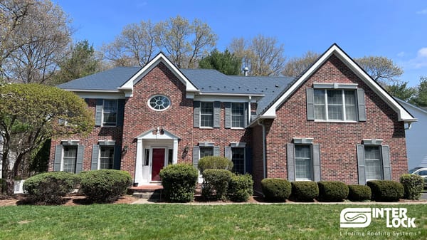 Two-story Colonial brick home in Sharon, MA with a steep multi-gable Interlock aluminum slate roof in Deep Charcoal, white trim, and red front door.