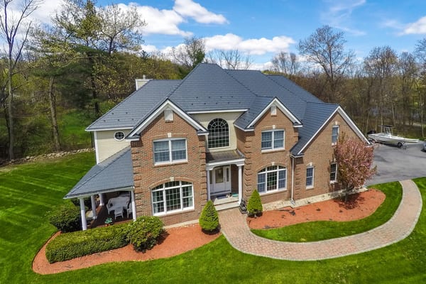 Aerial front view of a two-story brick Colonial home in Westford, MA with a complex multi-hip Interlock deep charcoal cedar shingle metal roof.