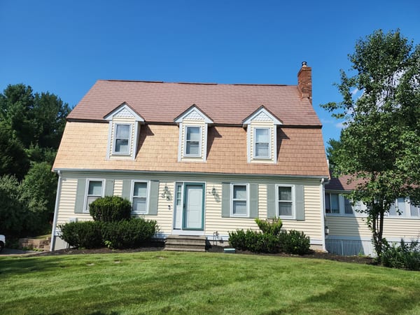 Aged Copper Interlock Shingle aluminum roof on a yellow two-storey Colonial home with dormers among tall, Wrentham, Massachusetts