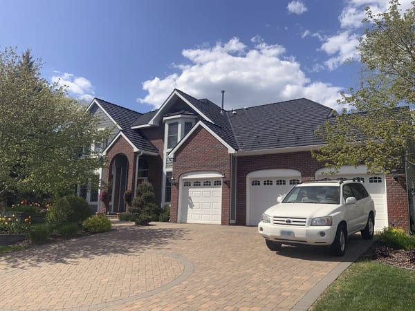 Two-story brick Colonial home in Eden Prairie, MN with black Interlock aluminum shake metal roof, multi-gable profile, and three-car garage on paver driveway.