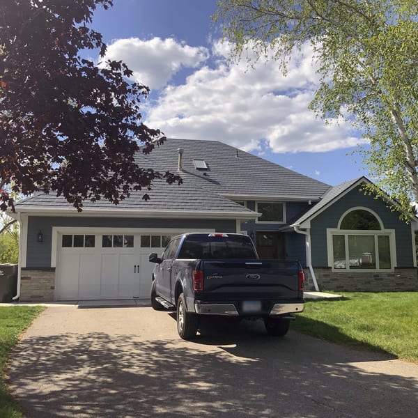 Charcoal grey Interlock aluminum slate metal roof on a blue Craftsman-style home in Eden Prairie, MN, featuring a skylight and multi-hip roofline.