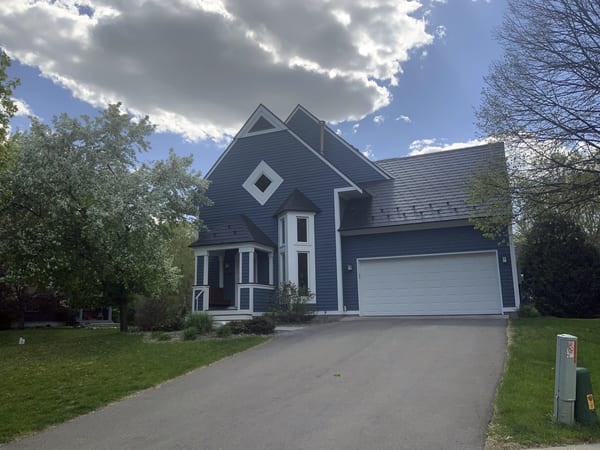 Two-story Victorian home in Eden Prairie MN with steep black Interlock aluminum slate roof, turret, multiple dormers, and blue-gray lap siding.