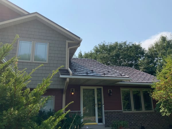 Tudor Brown Interlock Shake aluminum roof on a brown two-storey home with a metal roof in a forest, Northfield, Minnesota