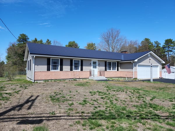 Ranch-style home in Concord, NH featuring a black Interlock aluminum slate metal roof with brick foundation, attached garage, and black shutters.